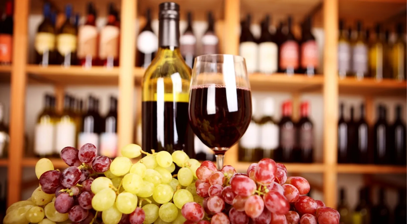Bottle of red wine and a full glass on a cellar-door counter with racked bottles behind
