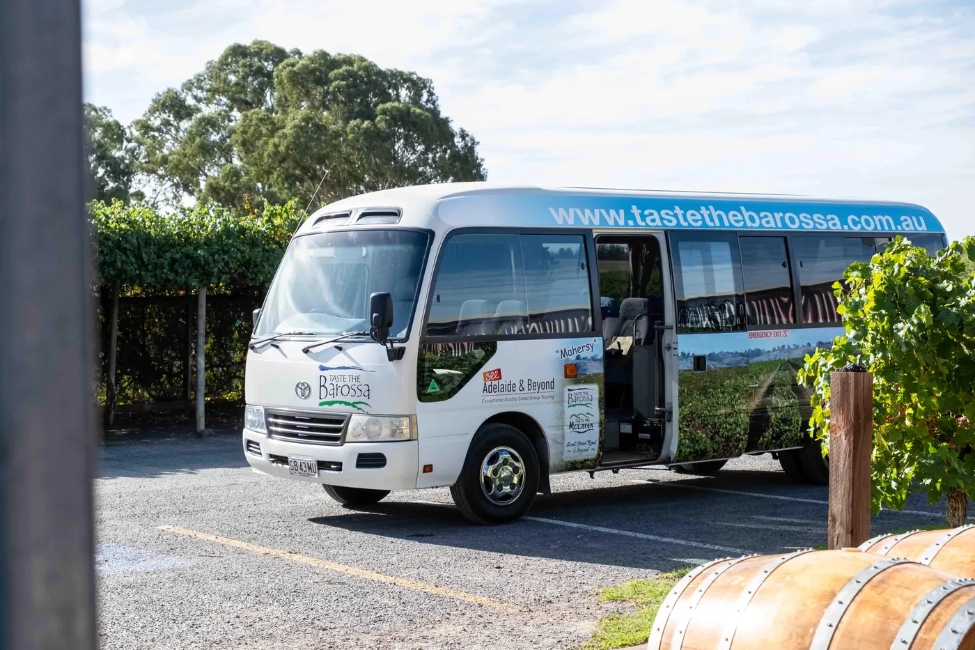 The Taste the Barossa 20-seat coaster parked beside old wine barrels at a Barossa cellar door