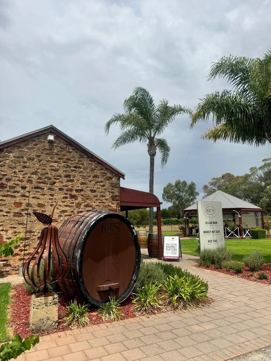 Bluestone cellar-door building with an old wine barrel and date palms at Kies Family Wines, Lyndoch