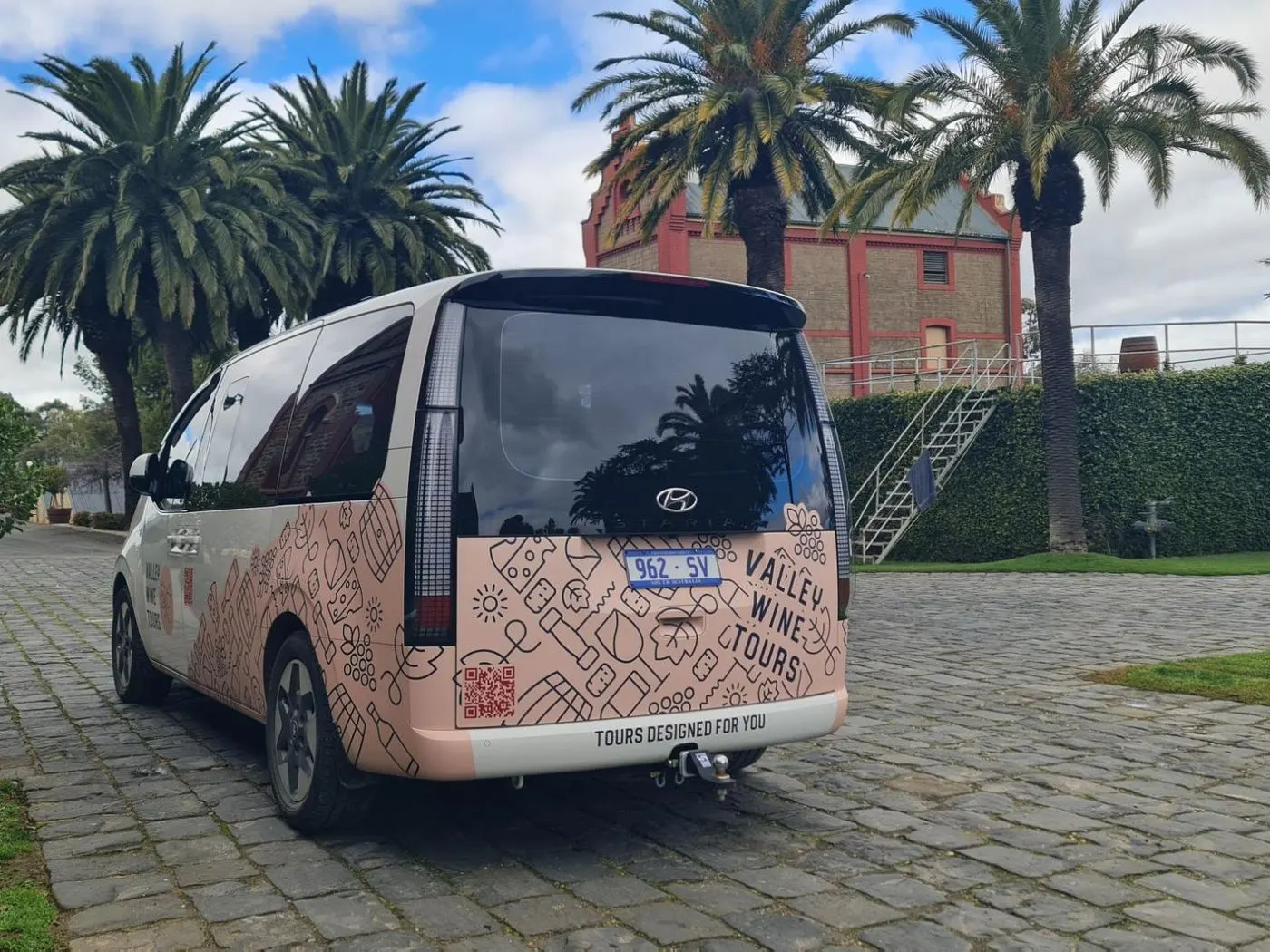 The tour's small branded van parked on cobbles under palm trees beside a Barossa winery