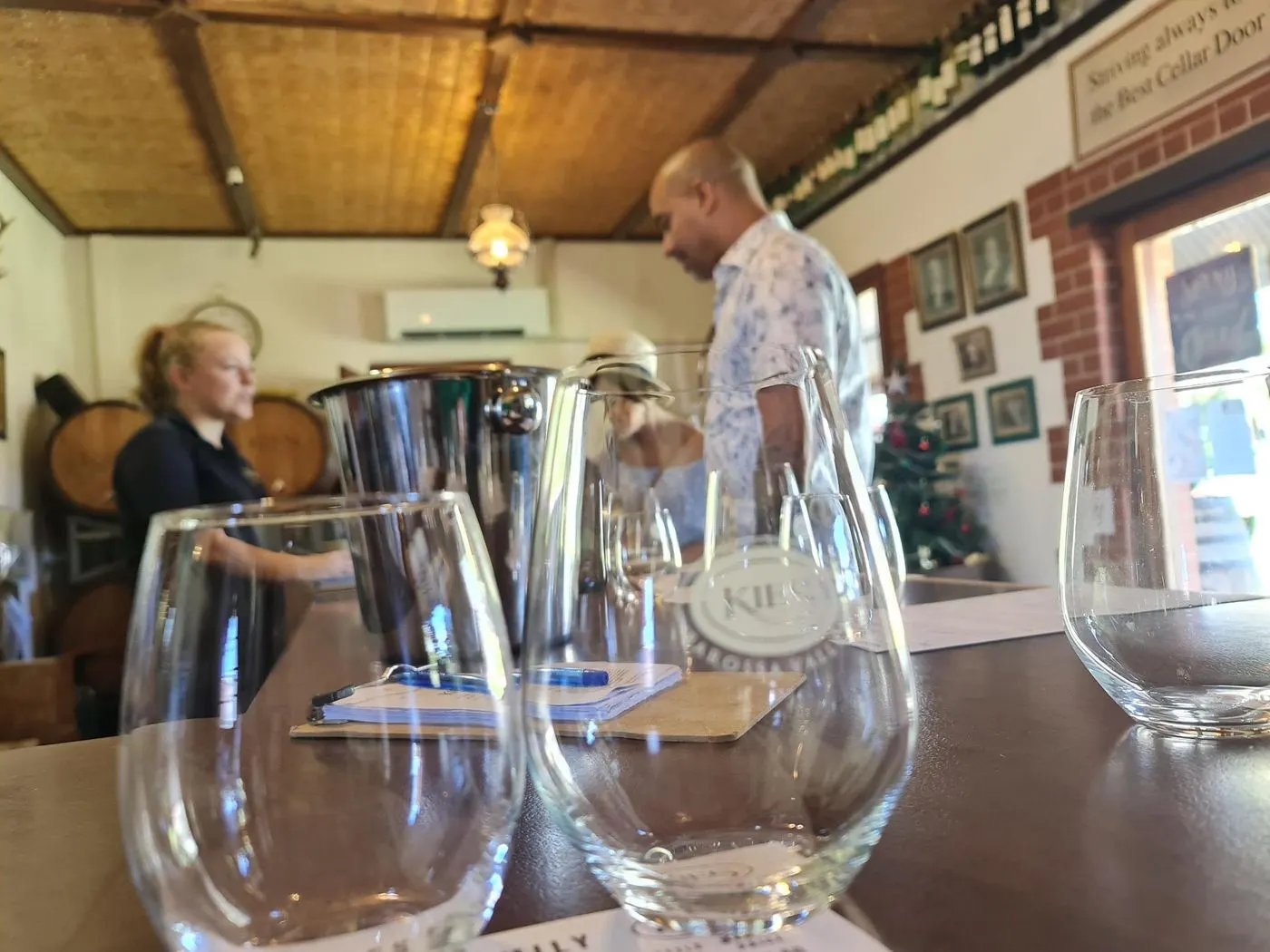 Empty tasting glasses on a cellar-door bench as a host pours behind the counter