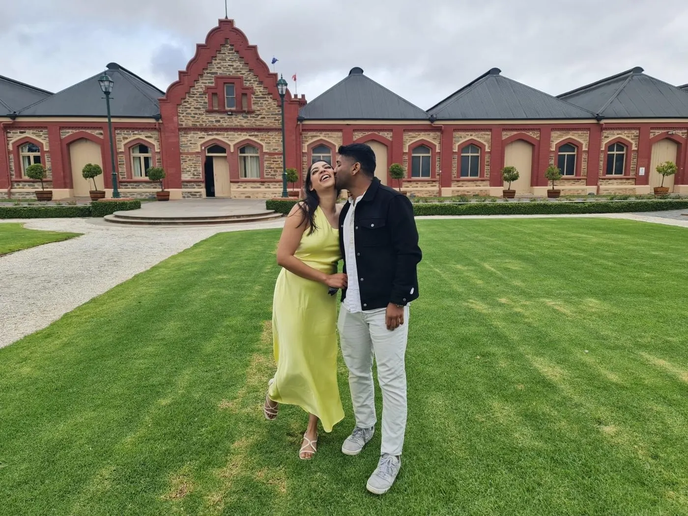 A couple on the lawn in front of a red-brick and bluestone Barossa winery