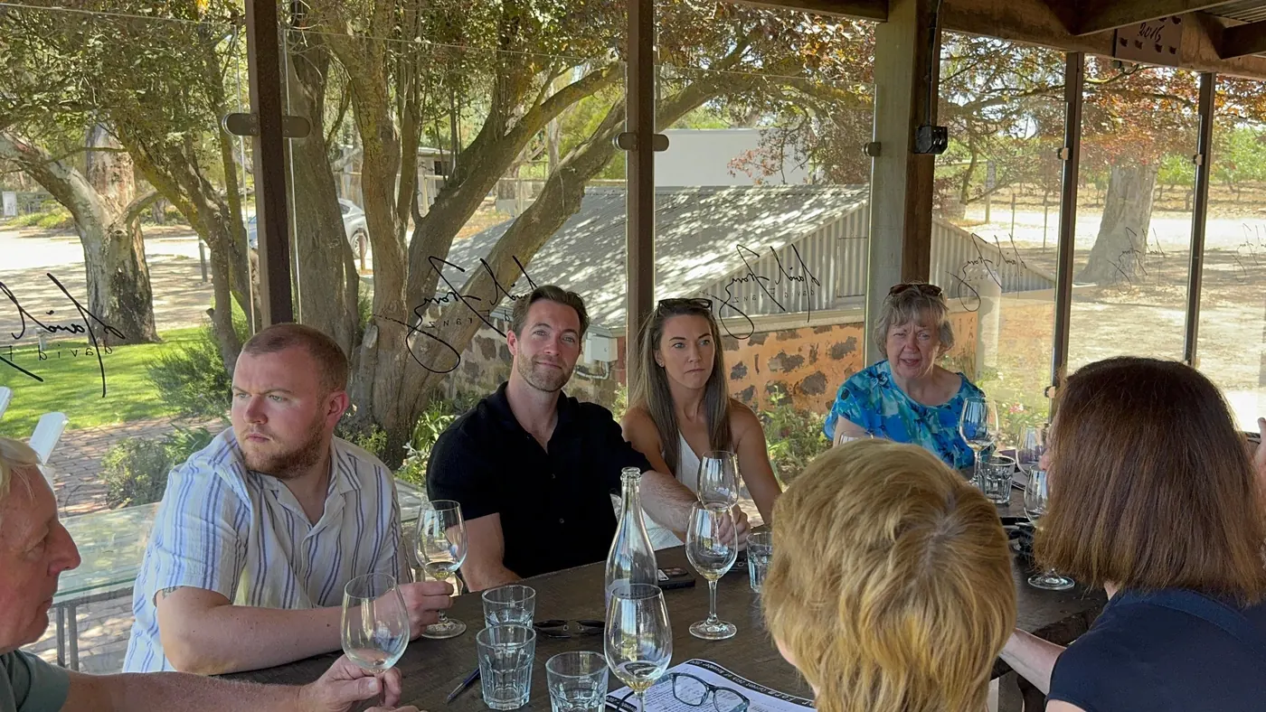 Guests tasting white wine at an outdoor table shaded by gum trees at a Barossa winery