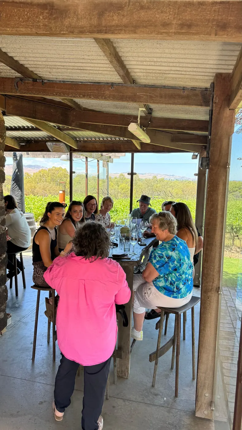 Long lunch table set with wine glasses in front of a wall of windows over the vineyard